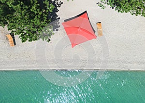 Aerial top view on the beach. Umbrellas, sunbeds, sand and ocean. Aerial view amazing empty white beach with red beach umbrella