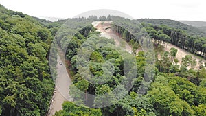 Aerial top view Car is driving on a bad road in the woods between the trees, bypassing potholes on the road.