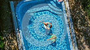 Aerial top view of children in swimming pool from above, happy kids swim on inflatable ring donuts and have fun in water