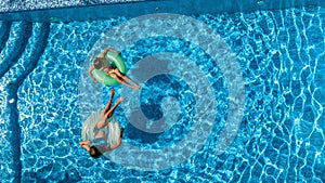 Aerial top view of children in swimming pool from above, happy kids swim on inflatable ring donuts and have fun in water