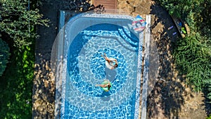 Aerial top view of children in swimming pool from above, happy kids swim on inflatable ring donuts and have fun in water