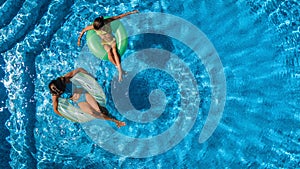 Aerial top view of children in swimming pool from above, happy kids swim on inflatable ring donuts and have fun in water