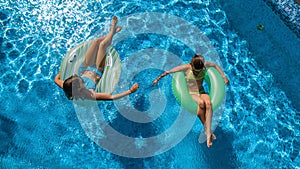 Aerial top view of children in swimming pool from above, happy kids swim on inflatable ring donuts and have fun in water