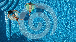 Aerial top view of children in swimming pool from above, happy kids swim on inflatable ring donuts and have fun in water