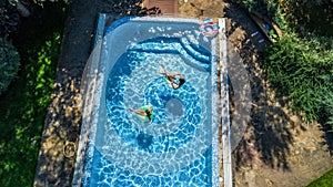 Aerial top view of children in swimming pool from above, happy kids swim on inflatable ring donuts in water on family