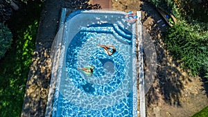 Aerial top view of children in swimming pool from above, happy kids swim on inflatable ring donuts in water on family