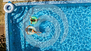 Aerial top view of children in swimming pool from above, happy kids swim on inflatable ring donuts in water on family