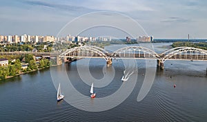 Aerial top view of Darnitsky bridge, yachts and boats sailing in Dnieper river from above, Kiev Kyiv city skyline