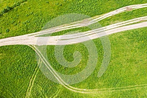 Aerial top view of dirt roads among green grass and meadows on bright sunny day. summer nature