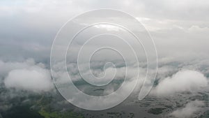 Aerial top view drone flies through fluffy rain clouds rolling over green forest by beautiful lake. Foggy morning in