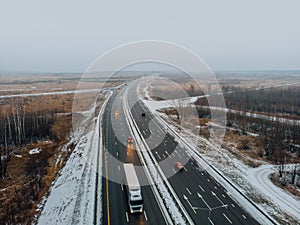 Aerial or top view from drone to winter asphalt highway or motorway road in countryside with car and truck traffic driving fast