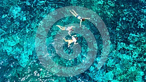 Aerial top view of family snorkeling from above, mother and kids snorkelers swimming in a clear tropical sea water with corals photo