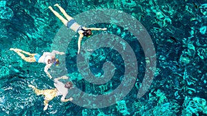 Aerial top view of family snorkeling from above, mother and kids snorkelers swimming in a clear tropical sea water with corals