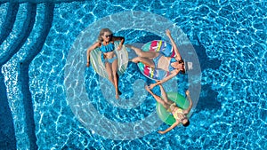 Aerial top view of family in swimming pool from above, happy mother and kids swim on inflatable ring donuts and have fun in water