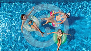 Aerial top view of family in swimming pool from above, happy mother and kids swim on inflatable ring donuts and have fun in water