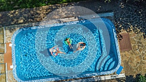 Aerial top view of family in swimming pool from above, happy mother and kids swim on inflatable ring donuts and have fun in water