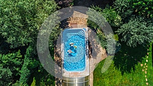 Aerial top view of family in swimming pool from above, happy mother and kids swim on inflatable ring donuts and have fun in water