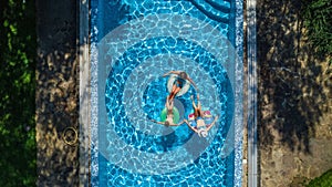 Aerial top view of family in swimming pool from above, happy mother and kids swim on inflatable ring donuts and have fun in water