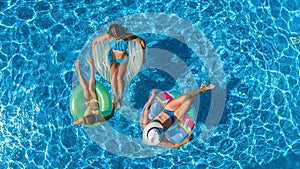 Aerial top view of family in swimming pool from above, happy mother and kids swim on inflatable ring donuts and have fun in water