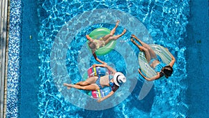 Aerial top view of family in swimming pool from above, happy mother and kids swim on inflatable ring donuts and have fun in water