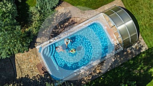 Aerial top view of family in swimming pool from above, mother and kids swim and have fun in water on family vacation