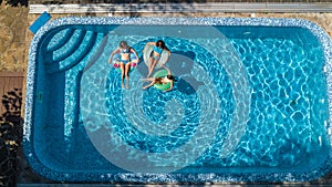 Aerial top view of family in swimming pool from above, mother and kids swim and have fun in water on family vacation