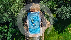 Aerial top view of family in swimming pool from above, mother and kids swim on inflatable ring donuts and have fun in water