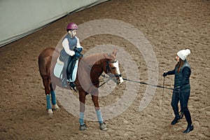 Aerial, top view. Female teacher, instructor teaching little girl, kid horseback riding. Outdoor lesson