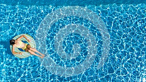 Aerial top view of girl in swimming pool from above, kid swims on inflatable ring donut , child has fun in water on vacation