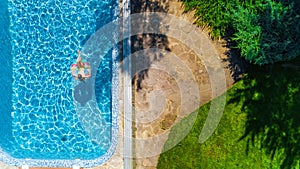 Aerial top view of girl in swimming pool from above, kid swims on inflatable ring donut , child has fun in water on vacation