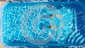 Aerial top view of girls in swimming pool water from above, active children swim, kids have fun on tropical family vacation