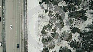 Aerial top view of a highway in winter weather with driving transport. Video. Snow covered ground and pine tree forest