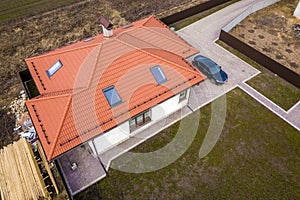 Aerial top view of house metal shingle roof with attic windows and black car on paved yard