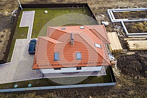 Aerial top view of house metal shingle roof with attic windows and black car on paved yard