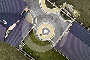 Aerial top view of house shingle roof on background of green lawn and colorful paved yard with geometrical abstract pattern.