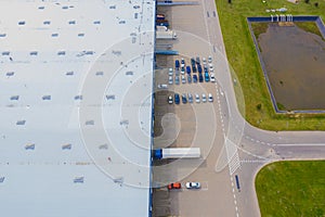 Aerial Top View of Industrial Storage Building Area with Solar Panels on the Roof and Many Trucks Unloading Merchandise