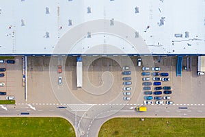 Aerial Top View of Industrial Storage Building Area with Solar Panels on the Roof and Many Trucks Unloading Merchandise