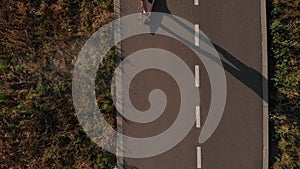 Aerial top view of man riding longboard at empty straight road. Summer vacation the guy rides skateboard at sunset time