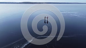 Aerial top view of A man teaches his girlfriend to skate on an open-air reservoir in winter, holding a hand. Clip.  People and out