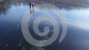 Aerial top view of A man teaches his girlfriend to skate on an open-air reservoir in winter, holding a hand. Clip.  People and out