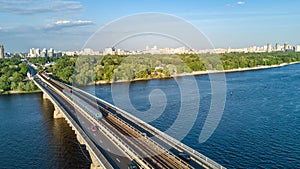 Aerial top view of Metro railway bridge with train and Dnieper river from above, skyline of city of Kiev