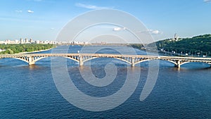 Aerial top view of Metro railway bridge with train and Dnieper river from above, skyline of city of Kiev photo