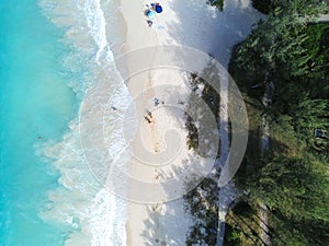 Aerial top view of the ocean with people on a sandy beach near the trees in Waimanalo, Oahu, Hawaii