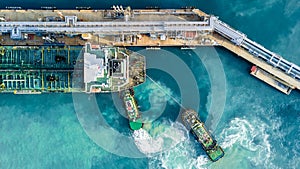 Aerial top view oil tanker ship at terminal industrial port tugboat drag crude oil tanker ship park to port for transfer crude oil