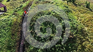 Aerial top view of racers riding a quad motorbike in the countryside through the muddy trail on green meadow. Stock