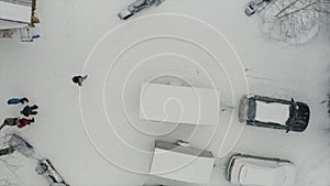 Aerial top view of a residential city courtyard after snowfall. Clip. Cars and snow mobiles covered by white snow on a