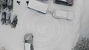 Aerial top view of a residential city courtyard after snowfall. Clip. Cars and snow mobiles covered by white snow on a