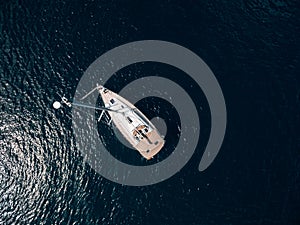 Aerial top view of a sailing yacht with a high mast floating on the water.