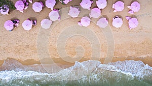 Aerial top view on the sandy beach. Pink umbrellas, sand, beach chairs and sea waves