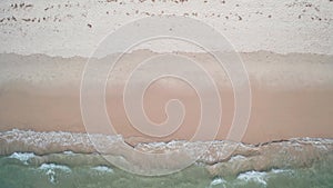 Aerial top view of sea waves crashing against the sandy beach